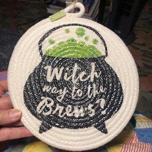 May include: White rope trivet with a black cauldron and green bubbling liquid. The text reads "Witch way to the Brew's?"