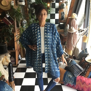 Peut inclure: Une femme portant une veste kimono bleu et blanc à motifs sur un pull blanc et un jean bleu. Elle se tient debout sur un sol à carreaux noirs et blancs.