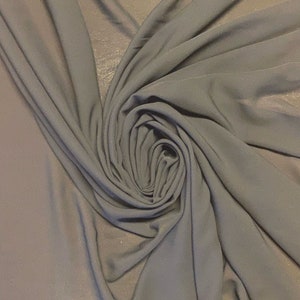 May include: A close-up of a gray fabric with a soft, flowing texture. The fabric is draped and folded, creating a swirling pattern.