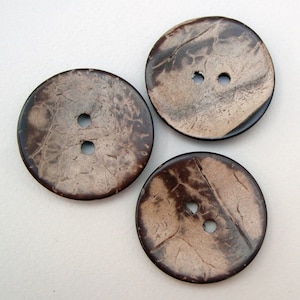 May include: Three brown coconut shell buttons with two holes each. The buttons have a natural, textured surface.