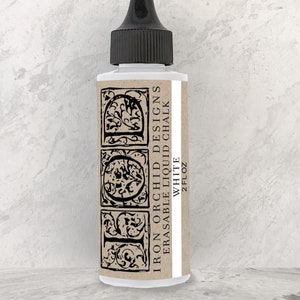 May include: A 2 fl oz bottle of Iron Orchid Designs Erasable Liquid Chalk in white. The bottle has a black cap and a label with the brand name and product information.