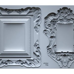 May include: Two silicone molds for making decorative picture frames. The molds are gray and feature intricate, ornate designs. The larger mold is 84 ml and weighs 128g. The smaller mold is 51 ml and weighs 77g. The text "FRAMES II IOD" is printed on the right side of the molds.