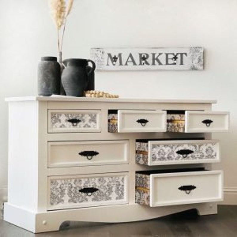 May include: White dresser with six drawers, some open, revealing patterned interiors. Black handles and a "MARKET" sign above. Two dark grey vases and a decorative vase with dried plants sit on top. The dresser is approximately 102 cm wide.