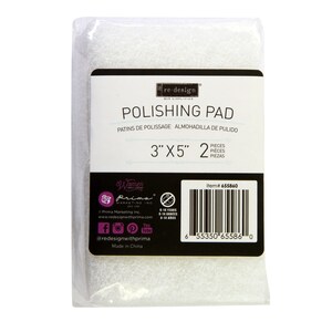 May include: A white polishing pad for crafts, measuring 3 inches by 5 inches. The package includes 2 pads. The packaging is white with black text and a barcode. The text on the package reads "re-design", "Polishing Pad", "Patins de Polissage", "Almohadilla de Pulido", "3"x5" 2", "Pieces", "Pieces", "Piezas", "Item# 655860", "Prima Marketing Inc.", "www.redesignwithprima.com", "0-14 Years", "0-14 Annees", "0-14 Años", "@redesignwithprima", "Made in China".