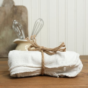 May include: A stack of white kitchen towels tied together with twine. The towels are folded and have a rustic, vintage look.