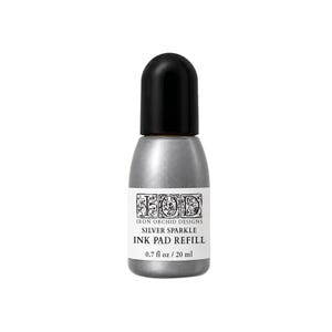 May include: A silver-colored ink pad refill bottle with a black cap. The white label features the text IOD Iron Orchid Designs, Silver Sparkle, Ink Pad Refill, and 0.7 fl oz / 20 ml. The bottle has a rounded shape and a metallic silver finish.