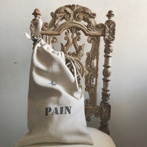 Puede incluir: Una bolsa de cordón de lino beige con una estrella y la palabra "PAIN" impresa en ella. La bolsa está sentada en una silla de madera tallada.