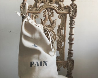 Puede incluir: Una bolsa de cordón de lino beige con una estrella y la palabra "PAIN" impresa en ella. La bolsa está sentada en una silla de madera tallada.