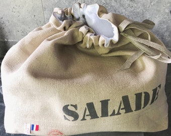 Puede incluir: Una bolsa de lino beige con cierre de cordón y una plantilla negra que dice "SALADE". La bolsa tiene una pequeña bandera francesa cosida en el lateral.