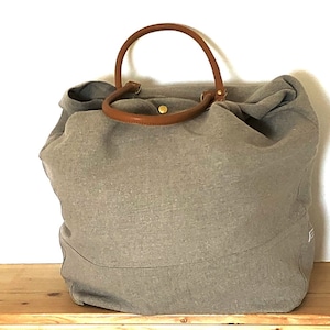 Puede incluir: Un bolso tote grande de lona gris con asas de cuero marr&oacute;n. El bolso tiene un dise&ntilde;o simple y cl&aacute;sico y es perfecto para llevar los art&iacute;culos esenciales del d&iacute;a a d&iacute;a.