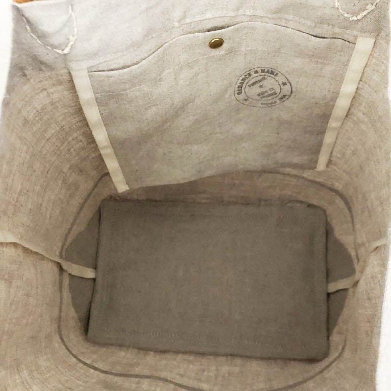 Puede incluir: Una bolsa de lona beige con un bolsillo interior grande y una peque&ntilde;a etiqueta redonda marr&oacute;n que dice "Vintage & Made" en letras blancas. La bolsa est&aacute; vac&iacute;a y el interior es visible.