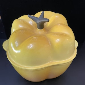 May include: Yellow ceramic bell pepper shaped casserole dish with a black knob on the lid.