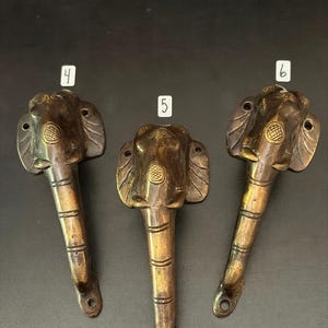 May include: Three antique brass elephant head door pulls. Each pull features an elephant head design with detailed ears and a textured trunk. The pulls are numbered 4, 5, and 6. The pulls are approximately 6 inches long.