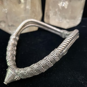 May include: A silver necklace with a detailed, intricate design. The necklace is made of twisted wire and has a pointed end.