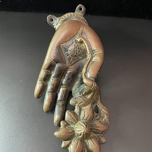 May include: A bronze hand sculpture with a flower design. The hand is open and the fingers are curled. The flower is a stylized lotus with a central bud.
