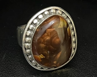May include: A silver ring with a brown agate gemstone set in a beaded oval bezel.