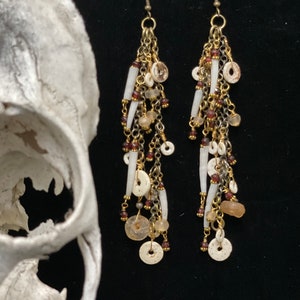 May include: A pair of long, dangling earrings with a bohemian style. The earrings feature a mix of white beads, gold chain, and small brown beads.
