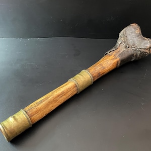 May include: A wooden club with a leather and metal head. The club is wrapped in brass bands.