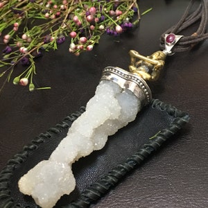 May include: A white crystal pendant with a silver and gold setting, hanging from a brown leather cord. The pendant is in a black leather pouch.