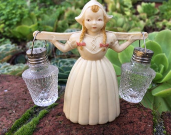 Salt and Pepper Shaker, Dutch girl with yellow braids with red bows. She is carrying a yoke with two clear glass lanterns with metal lids,