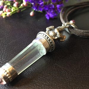 May include: A clear crystal pendant with a silver top and a small silver figurine on top. The pendant is attached to a brown leather cord.