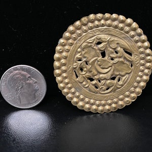 May include: A gold-toned metal decorative round ornament with a floral design. The ornament has a beaded border and a cutout floral pattern in the center.