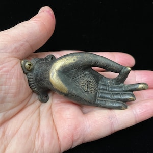 May include: A bronze hand sculpture with a gold finish. The hand is in a gesture of giving or receiving, with the palm facing up and the fingers slightly curled. The hand has a detailed design on the palm and fingers.