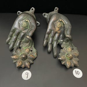 May include: Two antique bronze hand-shaped door handles with a floral design. The handles are in a dark green patina with gold accents. The handles are numbered 9 and 10.