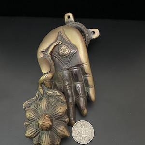 May include: A brass door knocker in the shape of a hand holding a flower. The hand is detailed with intricate carvings and the flower has a raised center.
