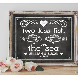 Può includere: Un cartello in ardesia nera con testo bianco che recita "Due pesci in meno nel mare, William & Susan 6.9.2018". Il cartello è incorniciato in una cornice bianca invecchiata e si trova su una superficie di legno con rose bianche di fronte.