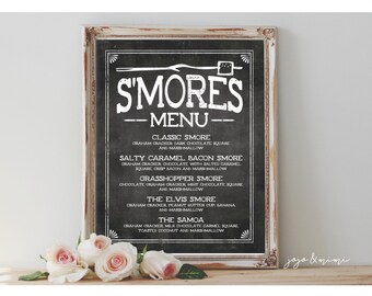 May include: A chalkboard sign with a white frame lists different s'mores variations with creative names like "The Elvis Smore" and "The Samoa". The sign is on a wooden surface with pink roses in front of it.