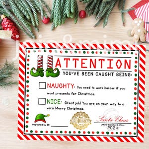 May include: A red and white striped card with a green elf hat and the text "ATTENTION YOU'VE BEEN CAUGHT BEING: NAUGHTY: You need to work harder if you want presents for Christmas. NICE: Great job! You are on your way to a very Merry Christmas. Santa Claus Official Signature S. Claus 2024 Inspected by Elf"