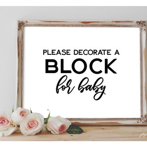 Könnte beinhalten: Ein gerahmter Druck mit dem Text "PLEASE DECORATE A BLOCK for baby" in Schwarz. Der Rahmen hat eine weiße und goldene Used-Optik. Weiche rosa und weiße Rosen sind am unteren Rand des Rahmens angeordnet.