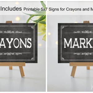 May include: Two black chalkboard signs with white text on wooden easels. The sign on the left says "Crayons" and the sign on the right says "Markers".