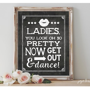 May include: A white framed chalkboard sign with black lettering that reads "... LADIES, YOU LOOK OH SO PRETTY NOW GET OUT &dance! ..." with a red lip print above the word "LADIES".
