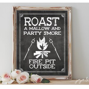 May include: A white sign with black text and a graphic of a campfire with marshmallows on sticks. The sign reads "Roast a Mallow and Party S'more Fire Pit Outside".