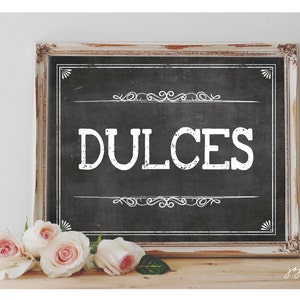 May include: A white sign with a black chalkboard background and a distressed white wooden frame. The sign says "DULCES" in white text with a decorative border.