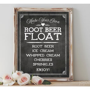 May include: A chalkboard sign with white text that reads "Make Your Own Root Beer Float" and lists the ingredients: root beer, ice cream, whipped cream, cherries, sprinkles, and enjoy. The sign is framed in white wood and has a distressed look.
