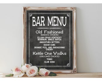 May include: A chalkboard sign with a white frame, listing a bar menu with the drinks "Old Fashioned" and "Kettle One Vodka".