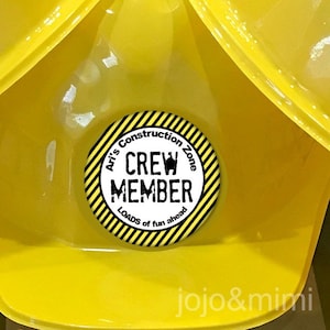 Może przedstawiać: Żółty kask budowlany z naklejką w czarno-żółte paski, na której widnieje napis "Ari's Construction Zone Crew Member Loads of fun ahead".