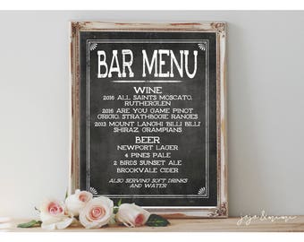 May include: A chalkboard sign with a white frame and the text "Bar Menu" in large white letters. The menu lists wine and beer options, including the year, type, and region of origin for each wine. The sign also includes the text "Also serving soft drinks and water."