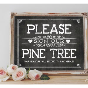 May include: A white sign with black text in a distressed white frame. The sign says "Please sign our pine tree. Your signature will become it's pine needles."