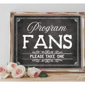 Puede incluir: Un cartel blanco con fondo de pizarra negra en un marco blanco desgastado. El cartel dice "Program Fans" en texto blanco con un adorno decorativo. Debajo del texto hay una pancarta blanca que dice "Please Take One".