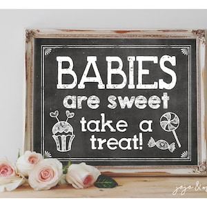 May include: A black chalkboard sign with white text that reads "Babies are sweet take a treat!"  The sign is framed in a distressed white wood frame. There are white drawings of a cupcake and a lollipop on the sign.