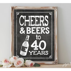 May include: A white sign with black lettering that reads "Cheers & Beers to 40 Years". The sign is framed in a white wood frame and has a bottle of beer drawn on it.