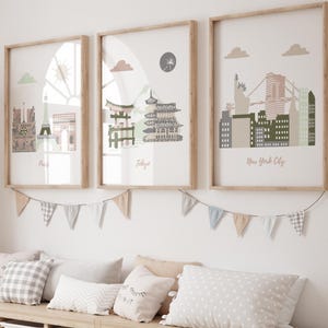 May include: A child's room with three framed prints depicting city skylines of Paris, Tokyo, and New York City. Below, a wooden storage unit with white bins is decorated with pillows and a giraffe ornament. A garland of triangular flags hangs above the unit.