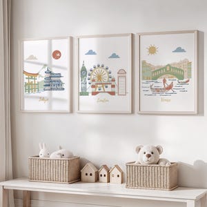 Peut inclure: Trois impressions encadrées de paysages urbains avec les noms Tokyo, Londres et Venise sous chaque image. Les impressions sont accrochées à un mur blanc au-dessus d'une table blanche avec deux paniers en osier et deux maisons en bois.