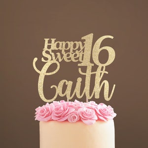 Peut inclure: Un topper de gâteau en paillettes dorées avec le texte "Happy Sweet 16 Caith" et des roses roses sur un gâteau blanc.