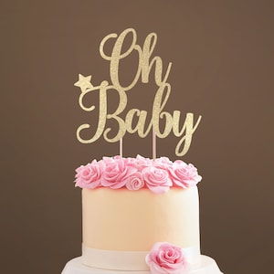 A cake topper made of gold glittered cardstock, spelling Oh Baby, decorated with butterflies. The font is hand-lettered typography.