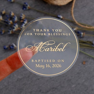 Könnte beinhalten: Ein runder, durchscheinender Aufkleber mit goldfarbenem Foliendruck, der den Text THANK YOU FOR YOUR BLESSINGS, den Namen Maribel in Schreibschrift sowie BAPTISED ON May 16, 2026 zeigt. Der Aufkleber hat einen dünnen Goldrand und eine glatte Oberfläche.